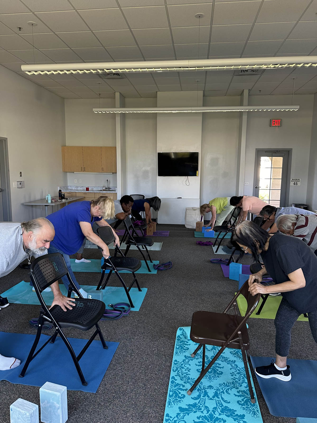 Multiple seniors doing chair yoga, bent over chairs